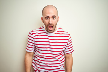 Young bald man with beard wearing casual striped red t-shirt over white isolated background In shock face, looking skeptical and sarcastic, surprised with open mouth
