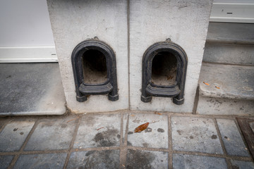 Boot scraper in a low wall at the entrance to the drive of a terraced house. Metal arch shaped with face top. Small cavity for mud behind frame.