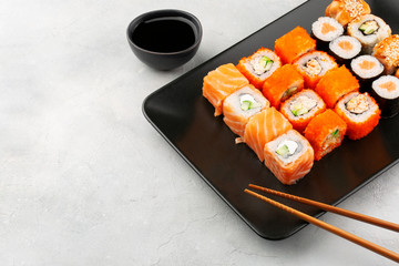 Japanese food. Sushi rolls with salmon, cream cheese, cucumber and other served on black plate with soy sauce, ginger and wasabi. Grey background copy space.