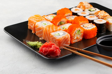 Japanese food. Sushi rolls with salmon, cream cheese, cucumber and other served on black plate with soy sauce, ginger and wasabi. Grey background copy space.