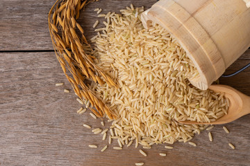 Brown rice or loonzain in wooden bucket and dry ear of rice or paddy isolated on old wood table...