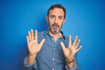 Handsome middle age senior man with grey hair over isolated blue background Moving away hands palms...