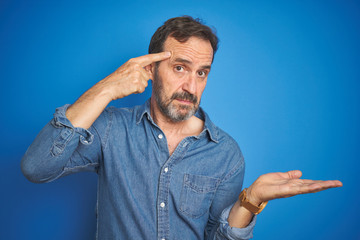 Handsome middle age senior man with grey hair over isolated blue background confused and annoyed...