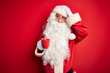 Senior man wearing Santa Claus costume holding cup of coffee over isolated red background stressed with hand on head, shocked with shame and surprise face, angry and frustrated. Fear and upset
