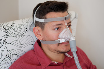 young white man with sleep apnea using CPAP machine and wearing nasal mask