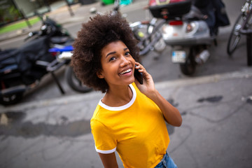 smiling african american young woman walking and talking with mobile phone on street