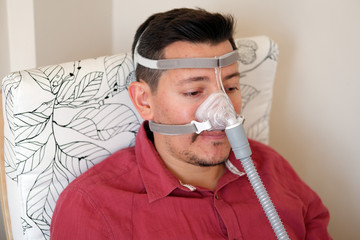 young white man with sleep apnea using CPAP machine and wearing nasal mask