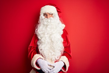 Middle age handsome man wearing Santa costume standing over isolated red background looking sleepy and tired, exhausted for fatigue and hangover, lazy eyes in the morning.