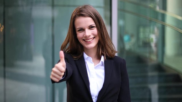 Confident young female manager outdoor in a modern urban setting giving thumbs up
