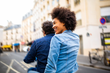 behind of young black woman sitting on back of scooter riding through city streets