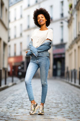 Full body of smiling young african american female fashion model standing on street in city denim jacket © mimagephotos