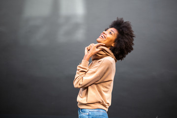 Side of attractive young black woman with afro hairstyle laughing by gray wall