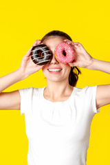 Beautiful girl makes glasses from donuts in the glaze. On a bright yellow background.