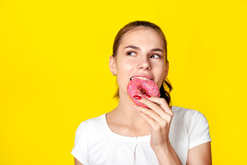 Beautiful girl eats a donut in pink glaze. On a bright yellow background.
