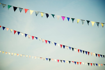 Strings of pennant flags in a variety of colors fluttering in soft sunny blue sky