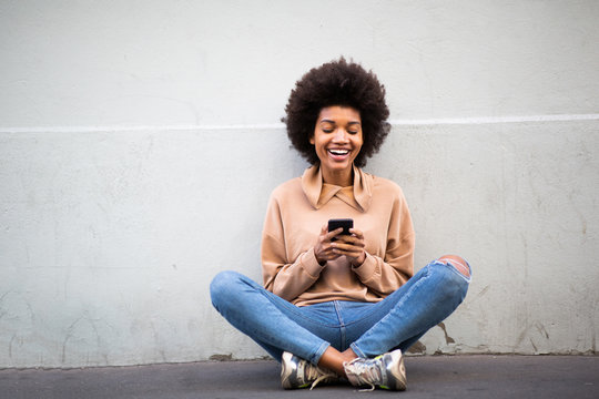 Happy Young African American Woman Sitting On Floor With Mobile Phone