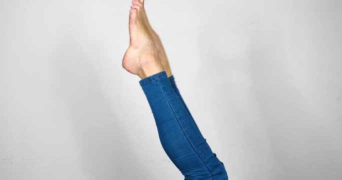A Pair of Upside Down Woman's Legs Wearing Tight Fitting Blue Jeans Stretching and Waving Isolated on White