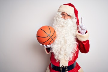 Senior man wearing Santa Claus costume holding basketball ball over isolated white background surprised with an idea or question pointing finger with happy face, number one