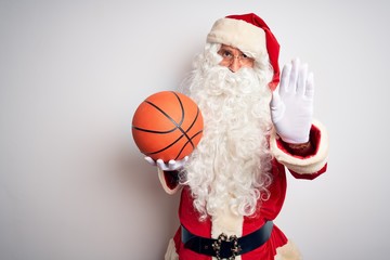 Senior man wearing Santa Claus costume holding basketball ball over isolated white background with open hand doing stop sign with serious and confident expression, defense gesture