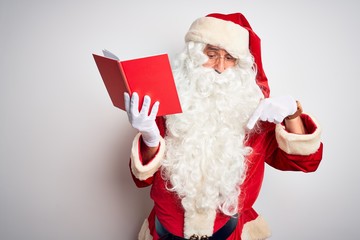 Middle age man wearing Santa Claus costume reading book over isolated white background Pointing down with fingers showing advertisement, surprised face and open mouth