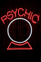 Psychic sign in red neon with a simple white crystal ball hanging in a dark window at night
