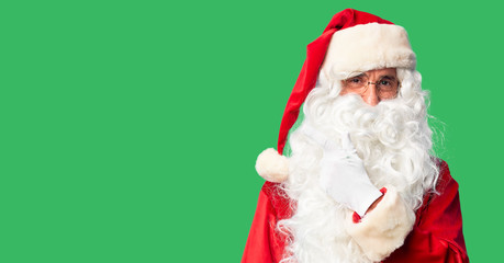 Middle age handsome man wearing Santa Claus costume and beard standing cheerful with a smile on face pointing with hand and finger up to the side with happy and natural expression