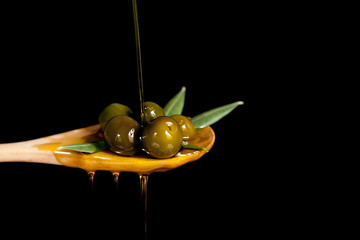 oil falling on handful of olives in wooden spoon close-up