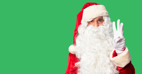 Middle age handsome man wearing Santa Claus costume and beard standing showing and pointing up with fingers number three while smiling confident and happy.