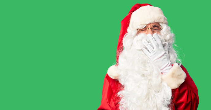 Middle age handsome man wearing Santa Claus costume and beard standing bored yawning tired covering mouth with hand. Restless and sleepiness.