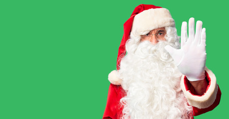 Middle age handsome man wearing Santa Claus costume and beard standing doing stop sing with palm of the hand. Warning expression with negative and serious gesture on the face.