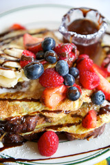 Mouthwatering close-up of brunch plate of gourmet french toast with bananas, raspberries, strawberries, blueberries and chocolate sauce
