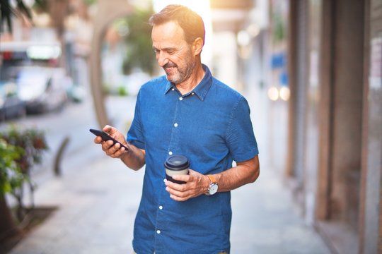 Middle age handsome businessman standing on the street using smartphone drinking take away coffee smiling