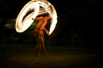 Unrecognizable shirtless male fire dancer twirling flaming torches at night on a dark beach
