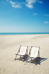 Pair of empty deck chairs sitting together on a deserted beach with calm blue sea on the  horizon
