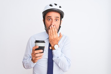 Middle age businessman wearing bike helmet drinking coffee over isolated white background cover mouth with hand shocked with shame for mistake, expression of fear, scared in silence, secret concept