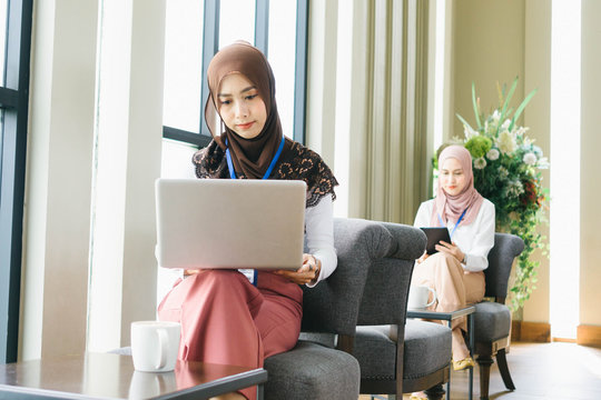 Two young muslim woman wearing hijab headscarf and using computer laptop in cafe.