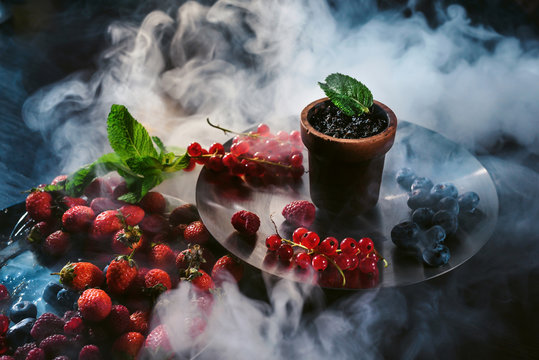 Tastes of hookah tobacco concept: raspberry, strawberry, blackberries, cranberries, black currants, wild berries. Hookah and fruits on dark wood table with shisha smoke clouds