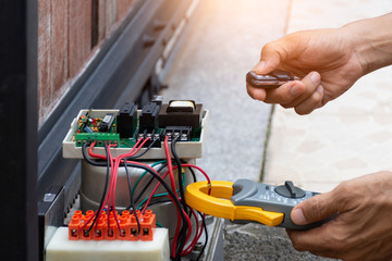 Technician man hand pressing remote control while repair and using digital clamp meter to test and...