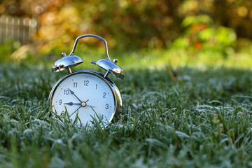 The alarm clock is in the grass covered with frost