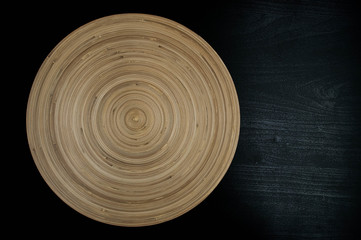 a large beige wooden plate with a spiral pattern on a black wooden table
