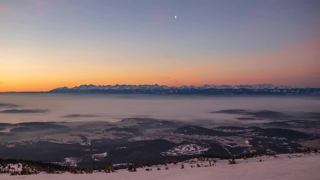 Sunrise over Tatra mountains seen from Babia mountain with cloud inversion and moon rising in the sky.