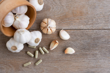 Fototapeta na wymiar Garlic bulb with cloves and garlic capsules isolated on wood table background. Natural herbal medicine plant and vitamin supplement concept. Top view. Flat lay. 