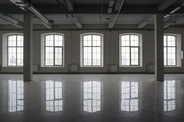 Empty large room in old factory building with row of big windows, columns and pipes under the beton...