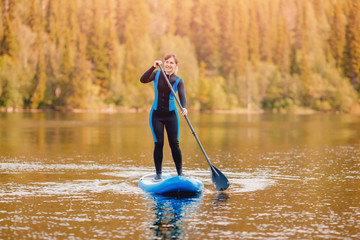 Girl in thermo clothing rowing oar on sup board blue lake water paddleboard background of forest