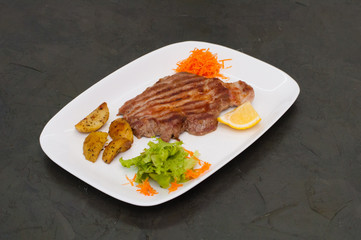 Juicy grilled meat steak with lemon, carrots, lettuce and potatoes.