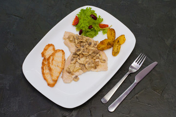 Stewed mushrooms with fish fillet, salad, fried potatoes and croutons, on a warm gray background. Tasty traditional italian food
