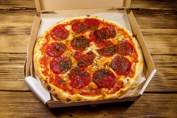 Delicious fresh pizza in cardboard box on a wooden table. Concept for home delivery of food, fast food, delivery of pizza