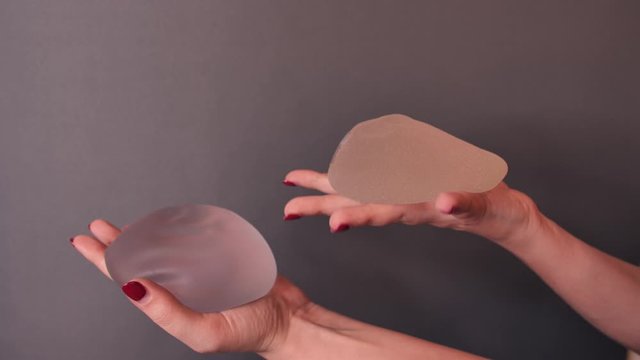 Girl shows, examines, squeeze, plays with different silicone implants for breast augmentation