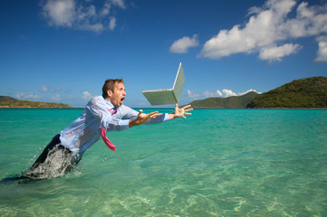 Shocked businessman leaping out of the water to catch his falling laptop computer in bright blue tropical sea