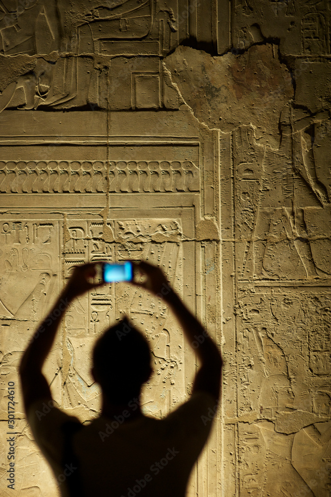 Canvas Prints silhouette of unrecognizable tourist taking photos with his smartphone in front of a panel of hierog